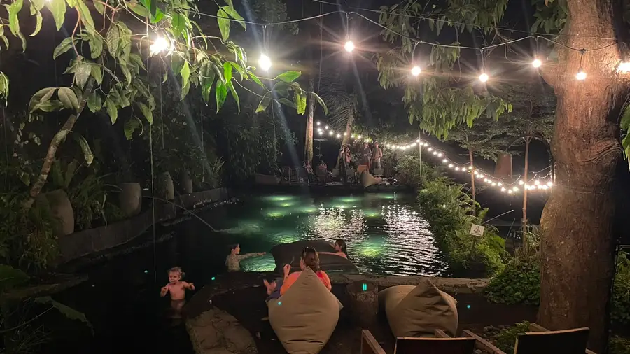 Community gathering by the natural pool, lit with string lights at night